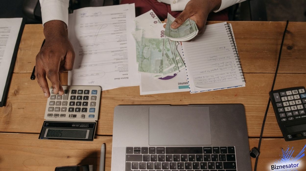 Osoba licząca banknoty nad biurkiem z kalkulatorem, laptopem i dokumentami